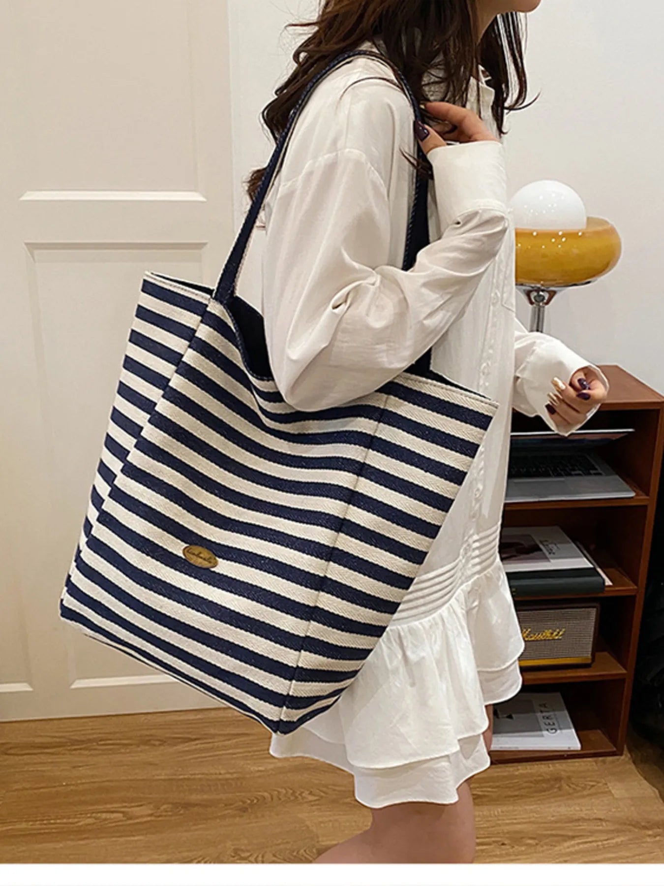 Person holding a blue and white striped tote bag in a room.