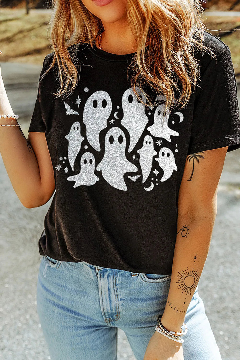 Person wearing a black t-shirt with ghost designs and light blue jeans outdoors.