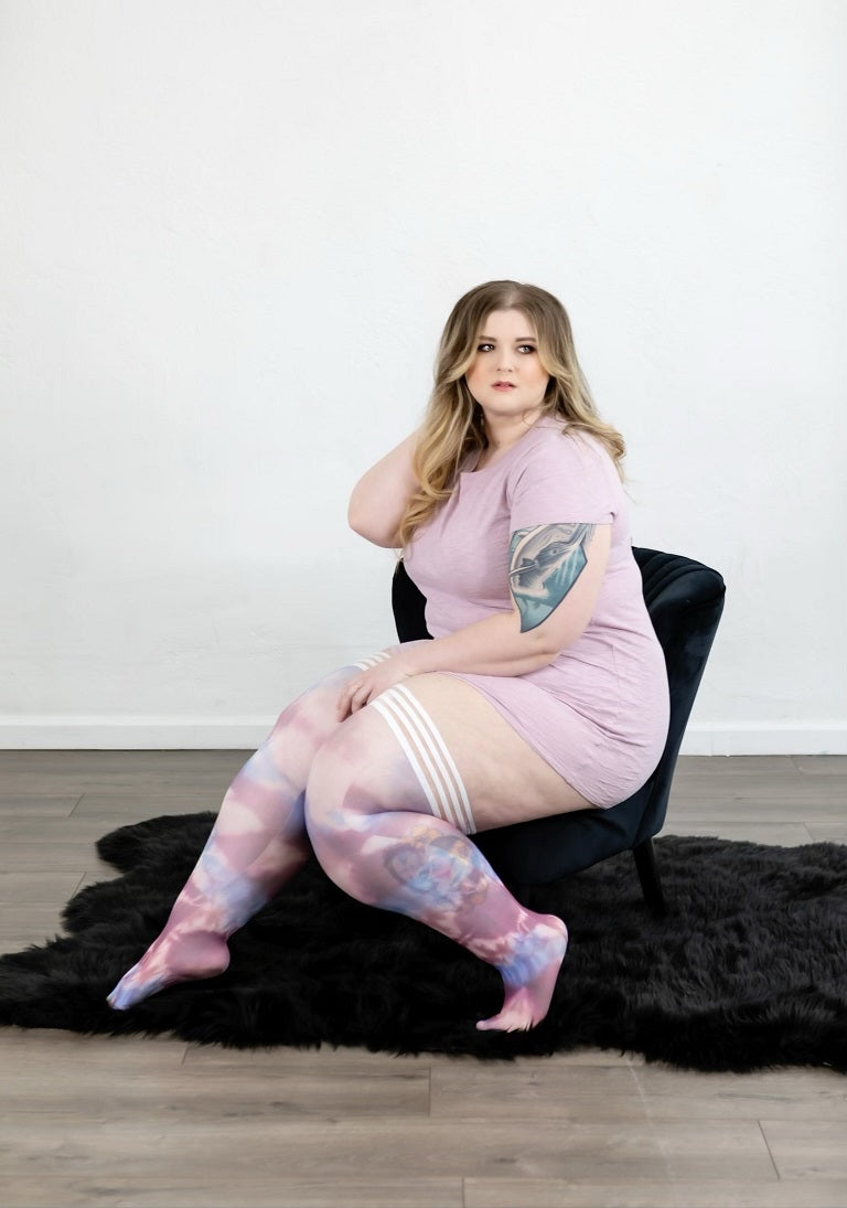 Woman sitting on a black chair wearing a pink dress and patterned stockings.