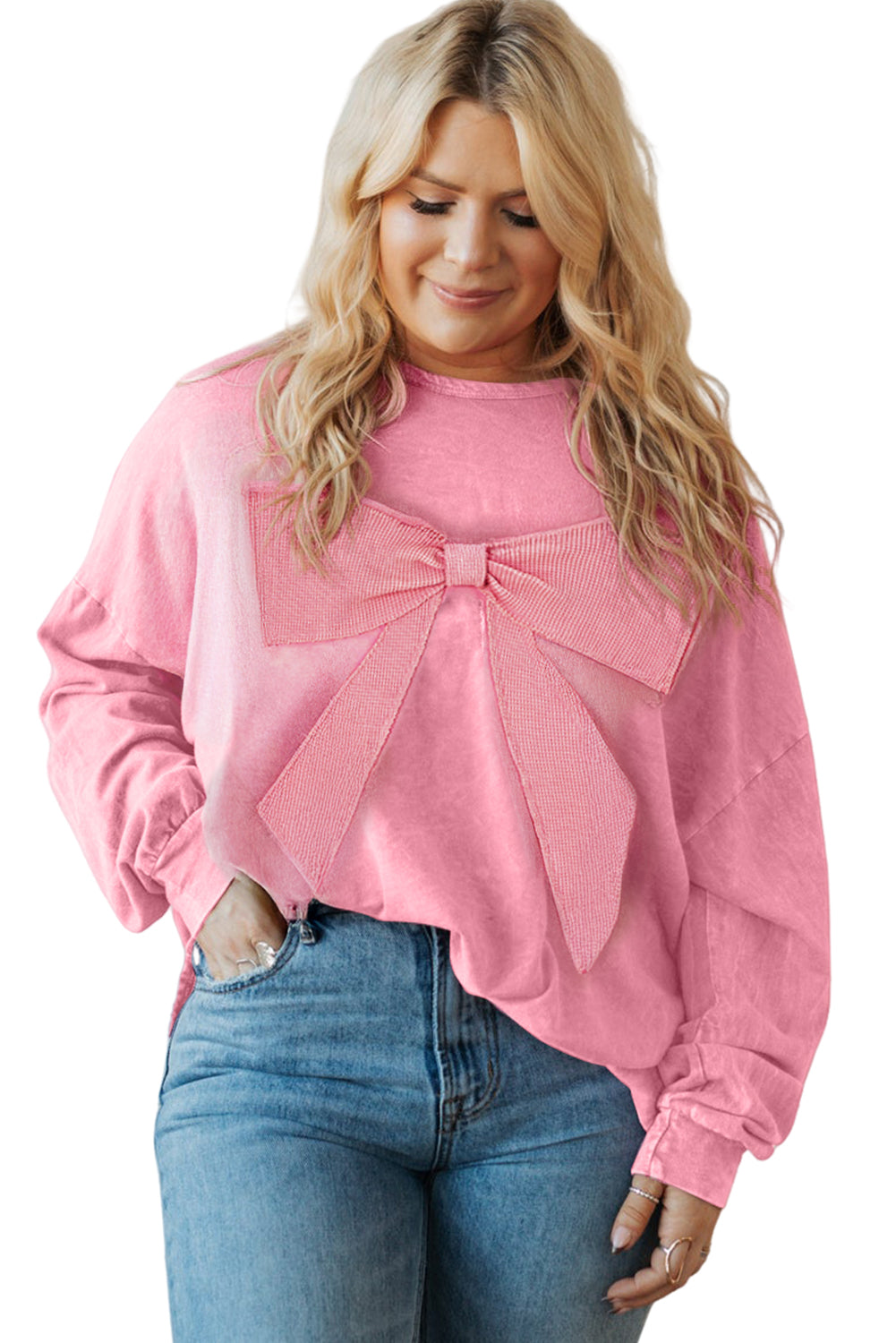 Woman wearing a pink sweater with a bow detail and blue jeans on a white background