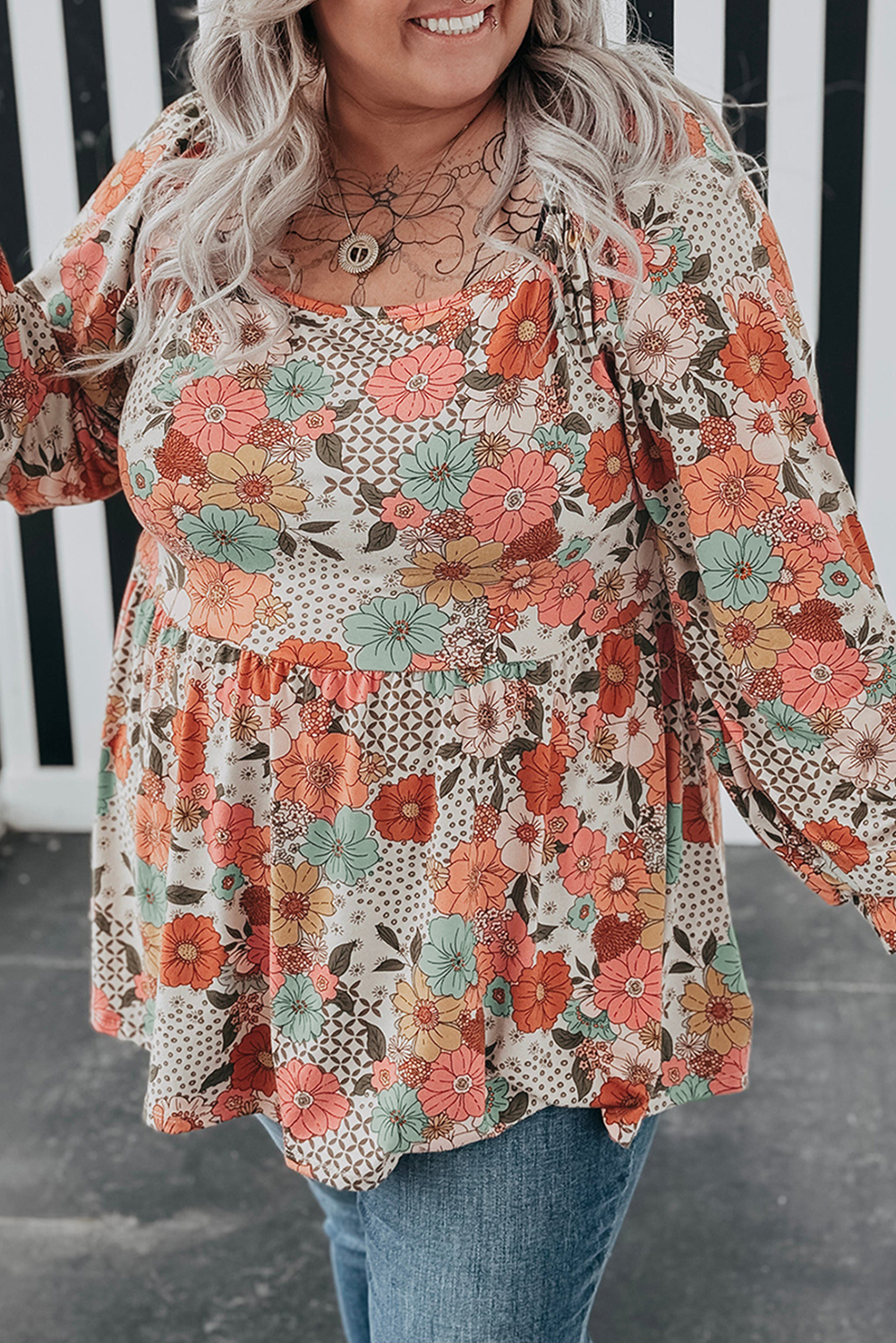 Woman wearing a floral blouse with long sleeves in front of a white picket fence.
