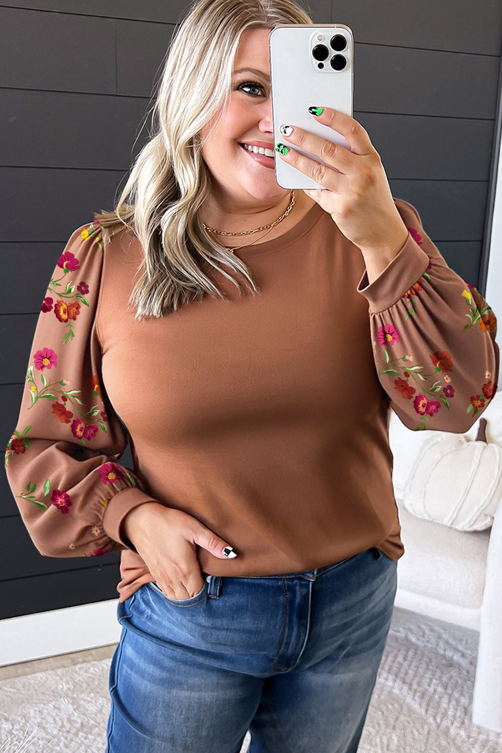 Woman taking a selfie wearing a brown blouse with floral sleeves and blue jeans.