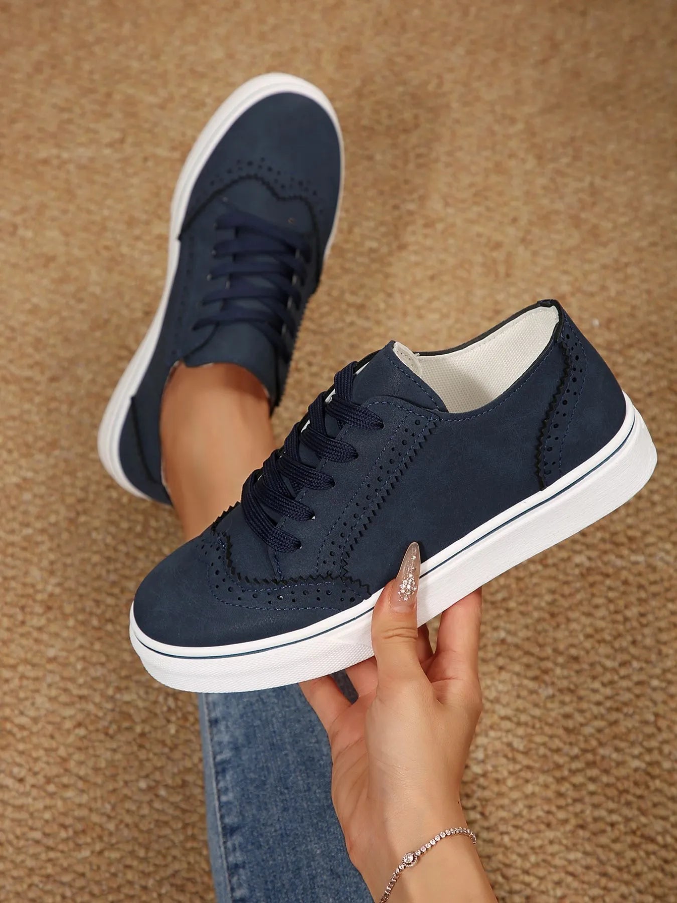 Navy blue sneakers with white soles held by a hand on a brown carpet background
