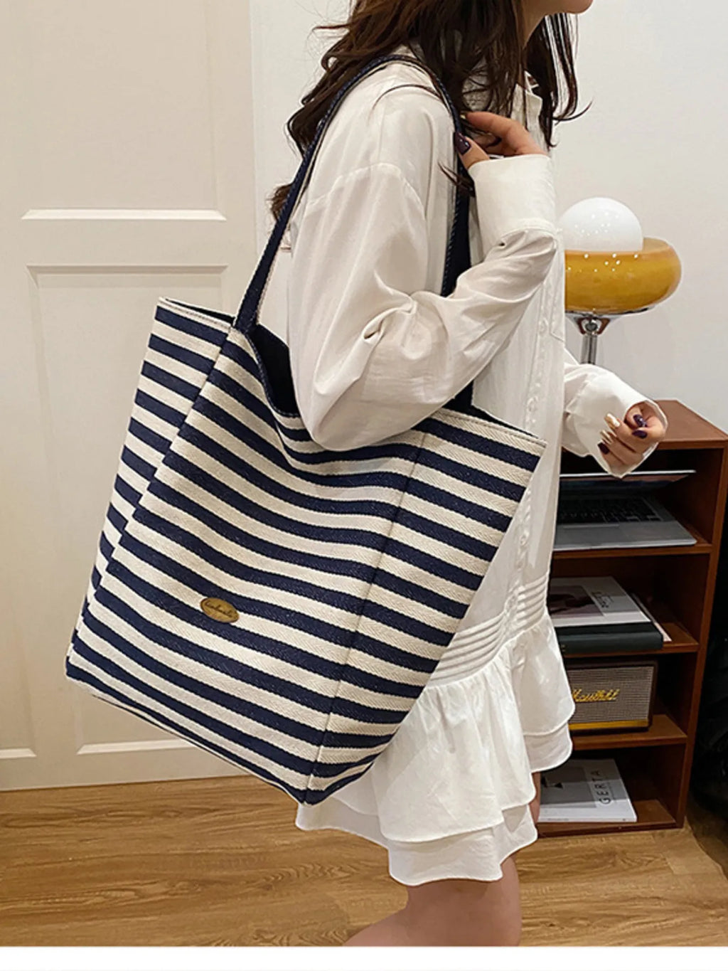 Person holding a blue and white striped tote bag in a room.