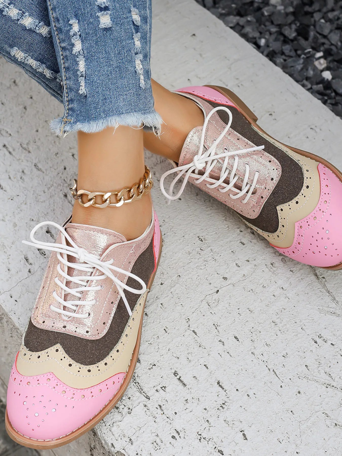 Pink and brown shoes with white laces worn by a person on a concrete surface.