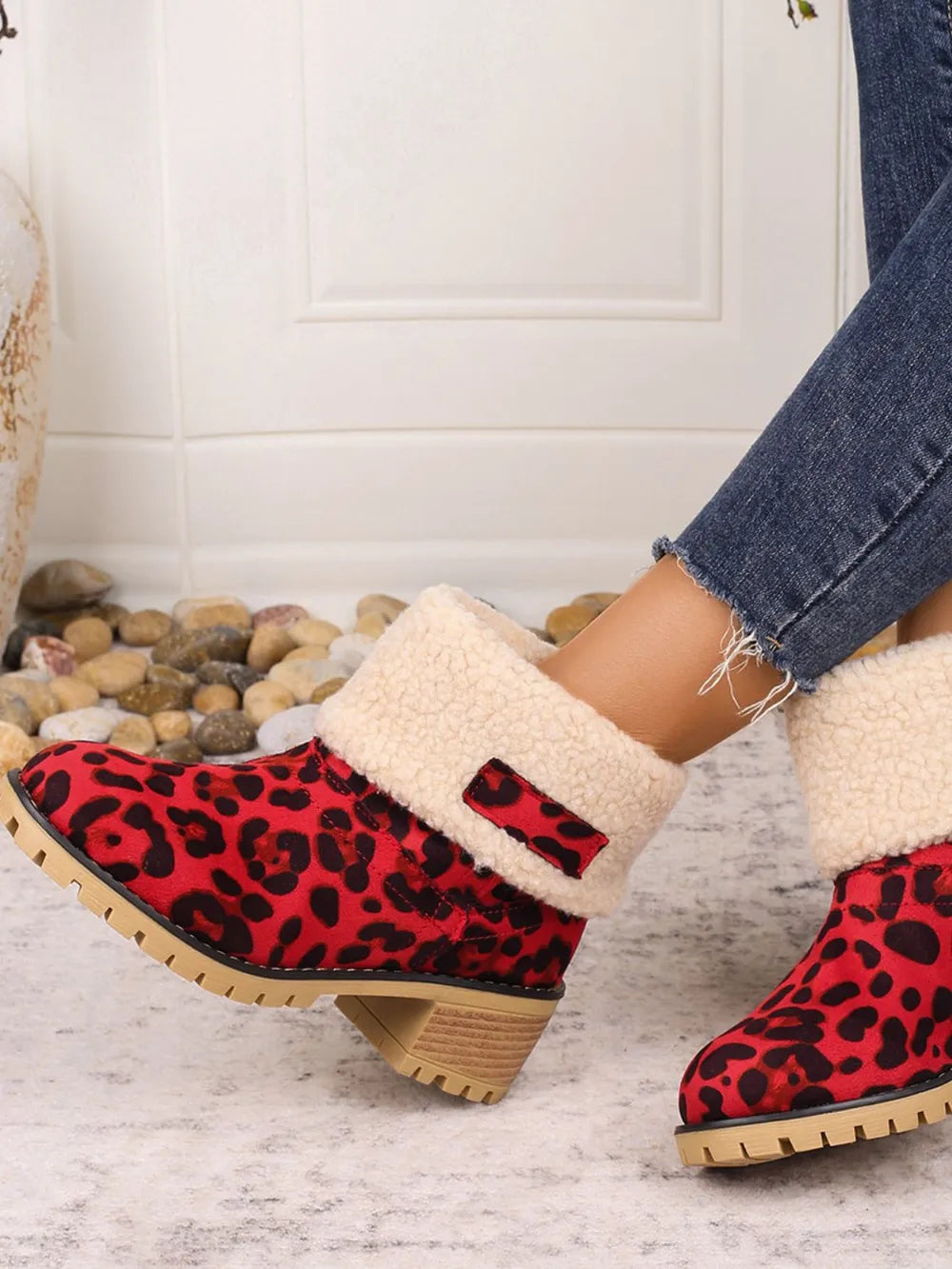 Red leopard print boots with beige fur lining worn indoors on a light wooden floor.