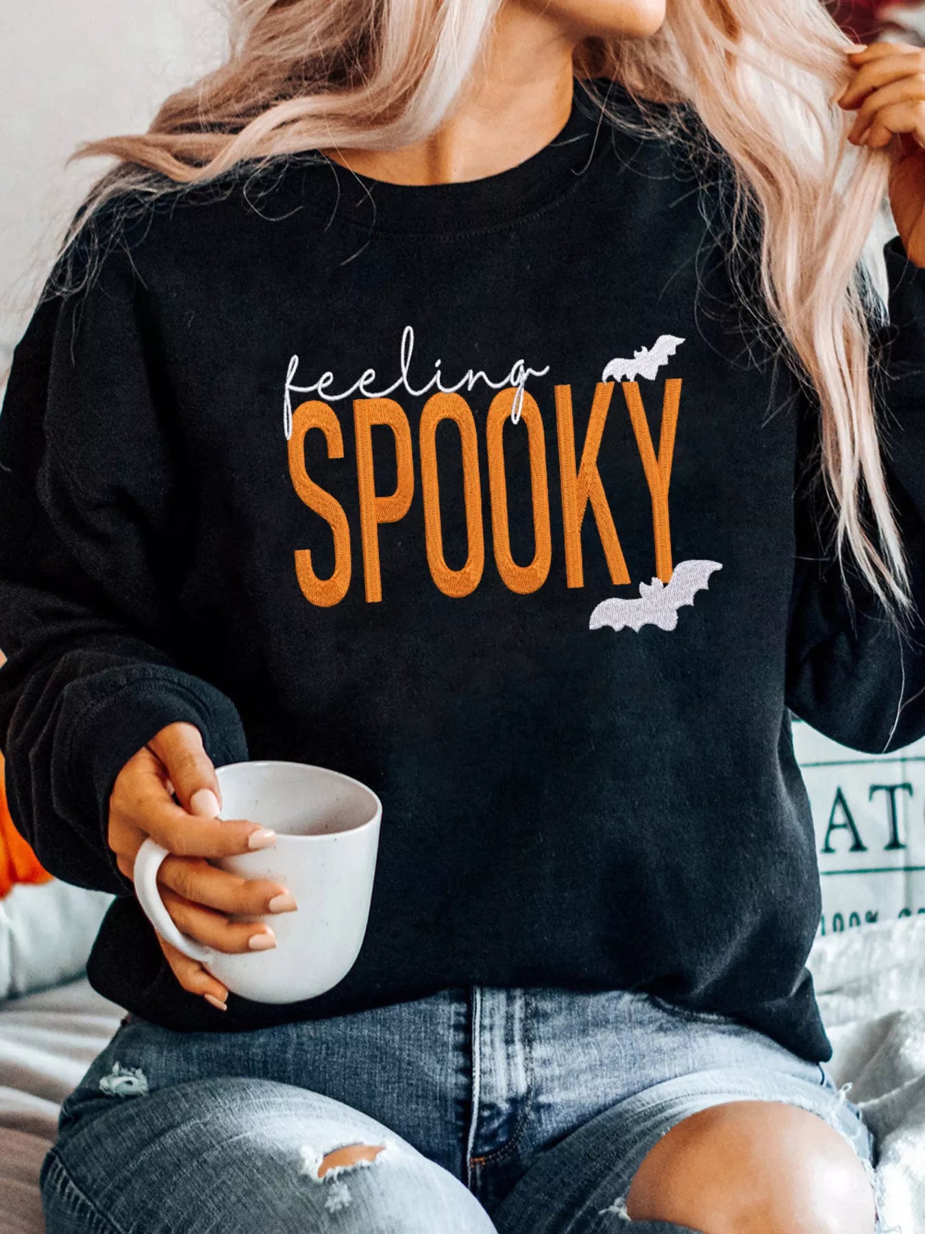 Person wearing a black sweatshirt with 'feeling spooky' text and holding a white mug.