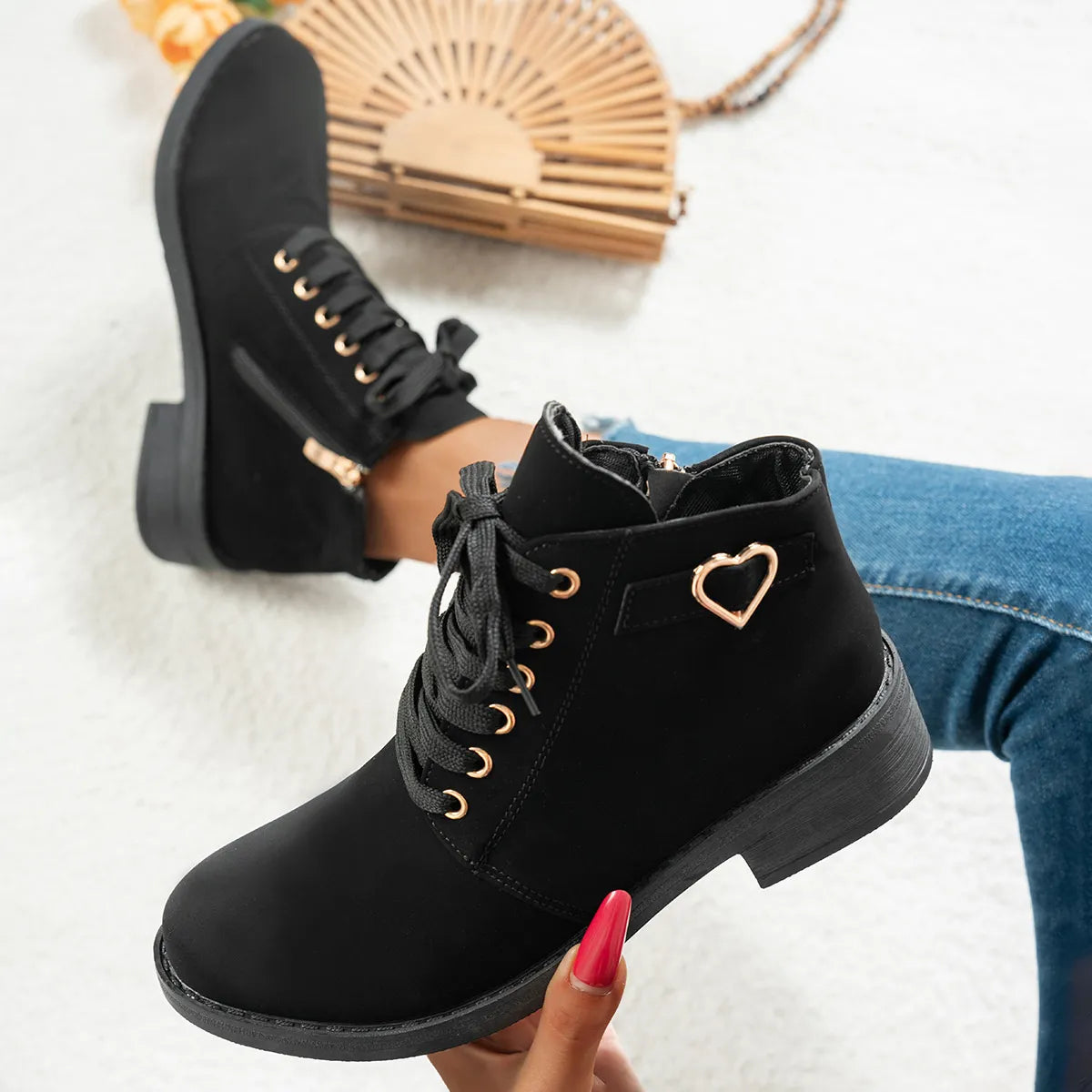Black ankle boots with heart detail held by a hand, with a blurred background