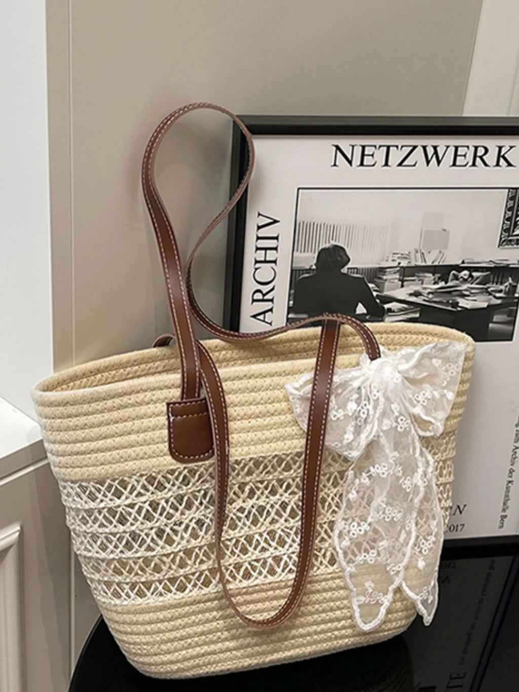 Woven handbag with lace detail in front of a framed picture