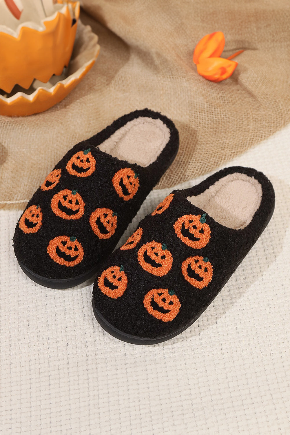 Black slippers with orange pumpkin patterns on a textured surface with Halloween decorations.