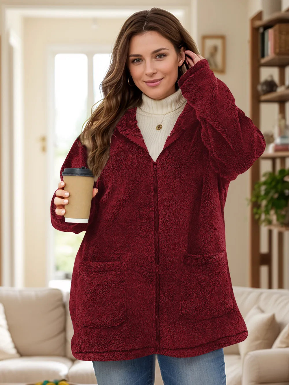 Woman wearing a red fleece jacket holding a coffee cup in a living room.