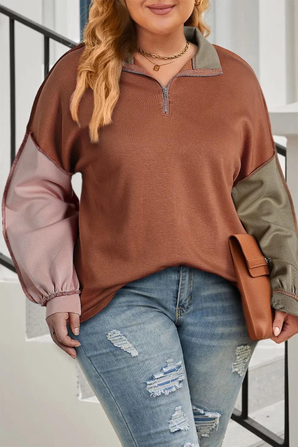 Woman wearing a brown and green color-blocked sweater with ripped jeans, holding a brown leather bag.