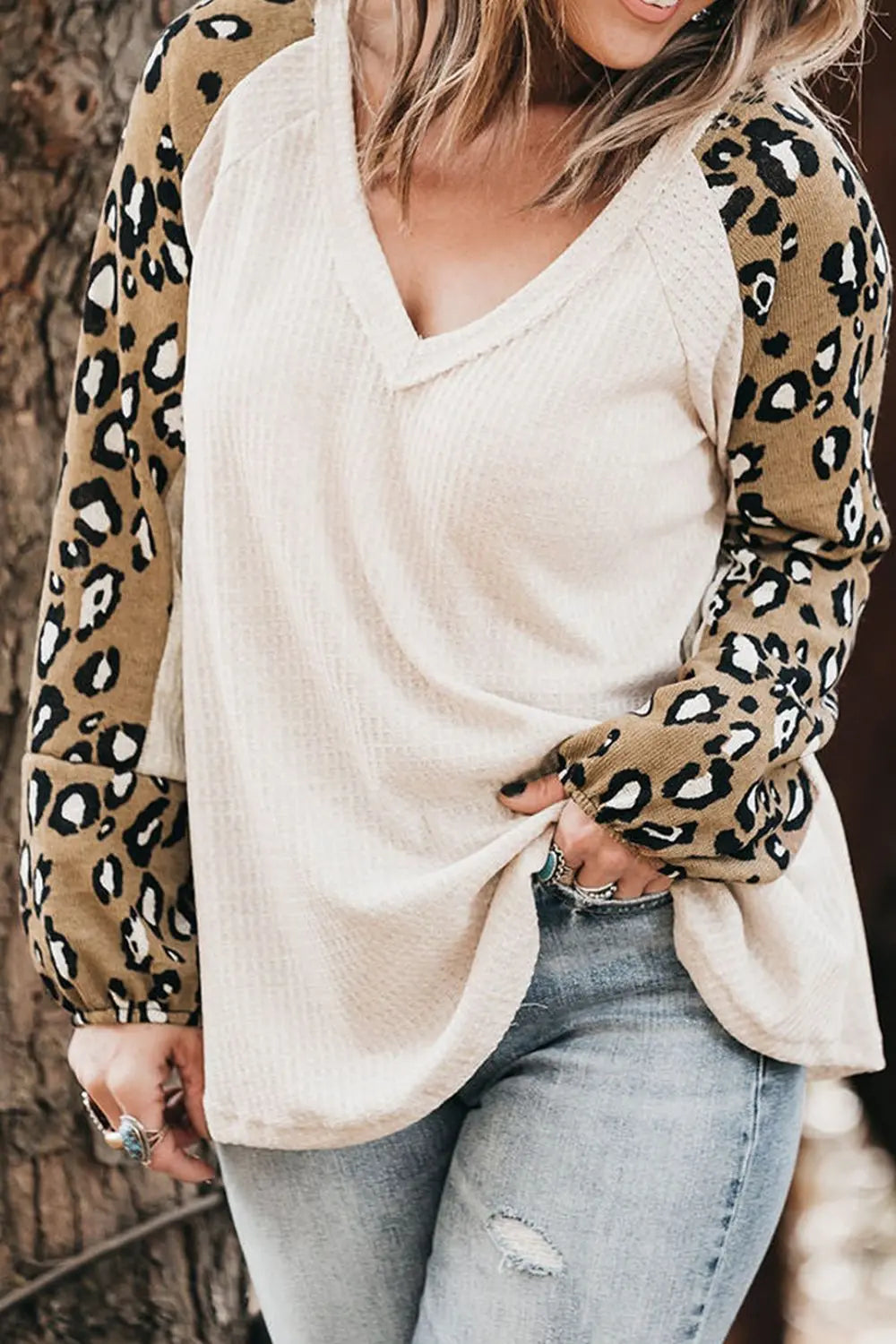 Person wearing a white top with leopard print sleeves and light blue jeans.